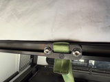 Close-up of a green strap attached to a metal bracket on a vehicle's roof rack.
