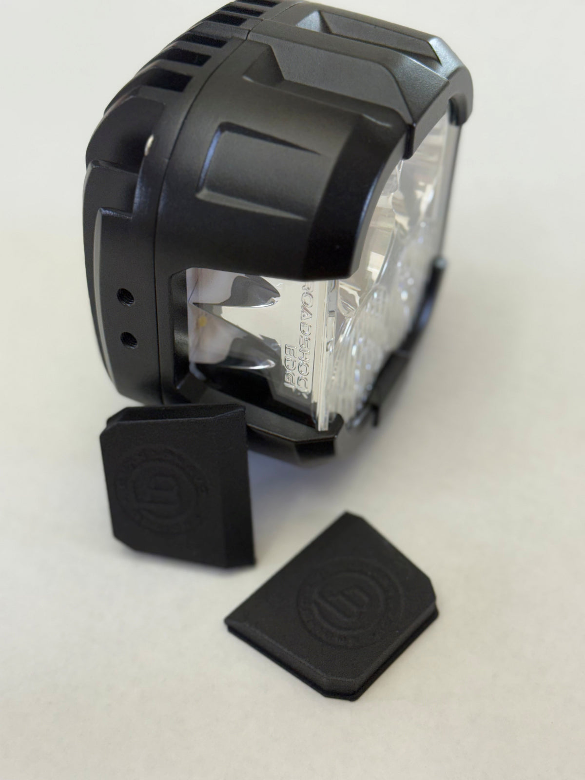Black motorcycle headlight with two black rubber covers on a light gray background