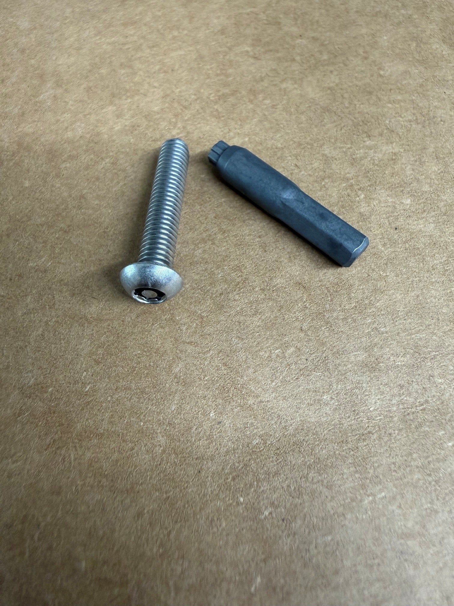 A silver metal threaded screw bolt and a dark gray hexagonal plastic or rubber insert placed on a brown textured cardboard background.