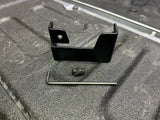 A black powder-coated metal bracket placed on a tailgate, with installation hardware including a bolt, washers, and nylock nut.