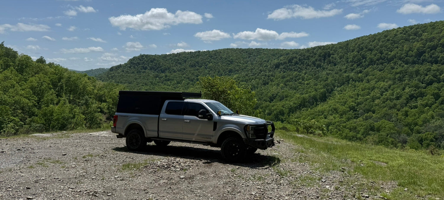 White pickup truck on a gravel road with green hills and blue sky in the background
