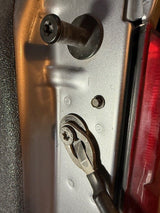Close-up of a metal panel with a screw and wrench, possibly from a vehicle.