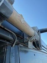 Close-up of a mechanical component with a wooden dowel and metal brackets against a blue sky.